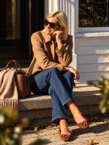 Angela seated on outdoor steps in a brown checked jacket, jeans and leopard ballet flats with pink trim.