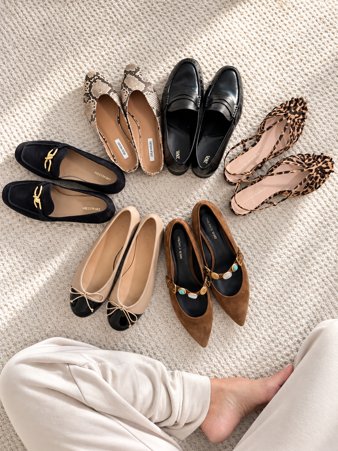 Six pairs of flats arranged in a circle on pale carpet, with loafers, two-tone ballet flats, snake-print mules and leopard slingbacks.