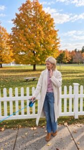 Angela Howenstein wearing a light coat over a pink sweater with wide-leg jeans and tan ankle boots outdoors in autumn.