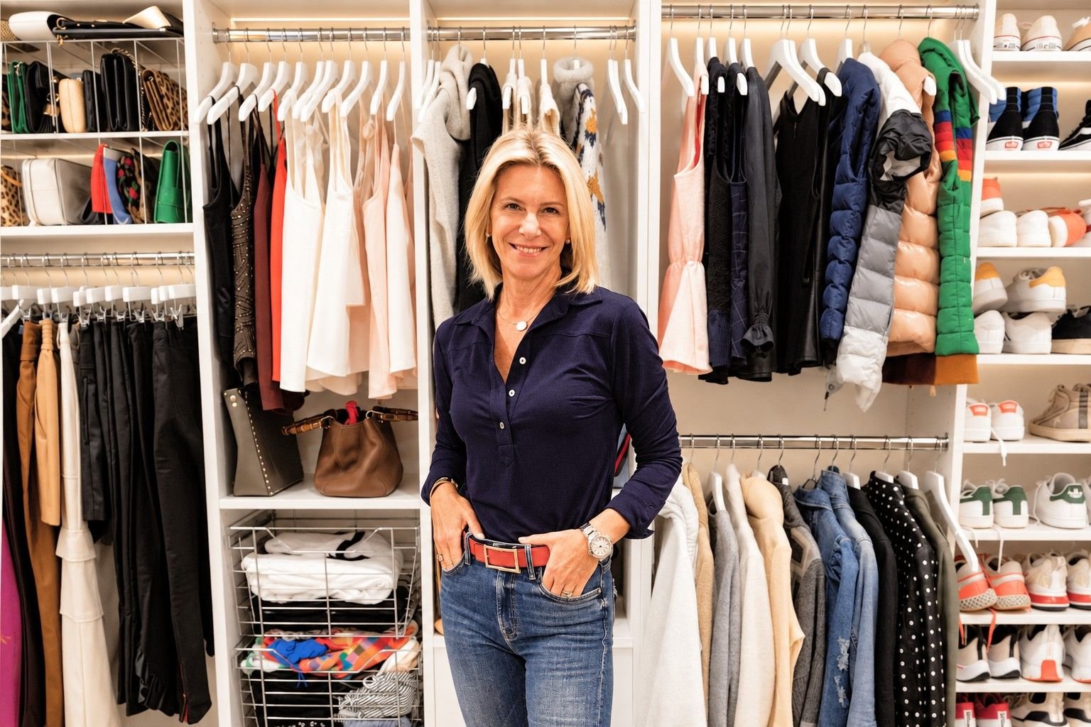 Angela Howenstein standing in her organized closet wearing a navy blouse and jeans.