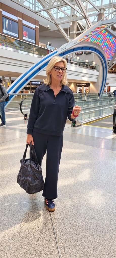 Angela Howenstein wearing a navy zip-neck top and matching pants with sneakers and a tote.
