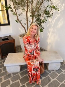 Angela Howenstein seated in a red and cream printed long dress.