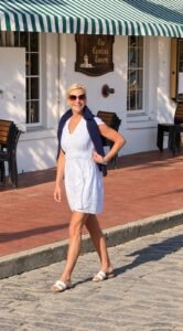 Angela Howenstein wearing a white eyelet dress with a navy layer draped over her shoulders and flat sandals.