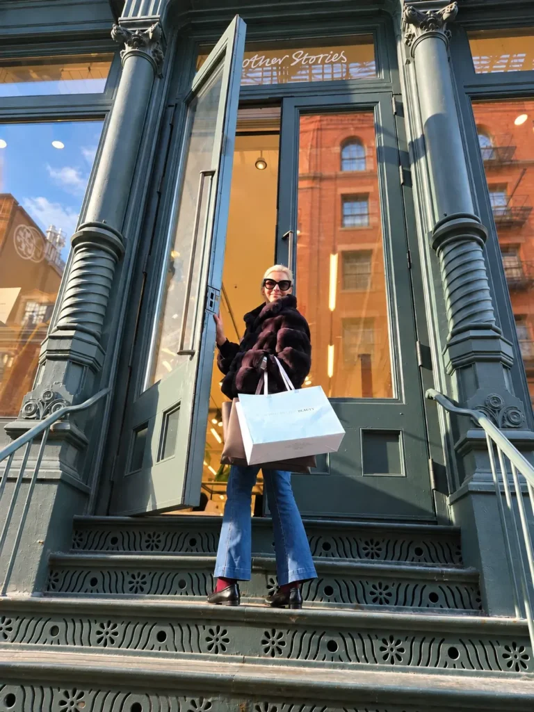 Angela Howenstein wearing a plaid jacket and blue jeans while carrying a shopping bag outside a store.