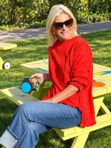 Angela Howenstein wearing a red long-sleeve top and cuffed jeans while seated outdoors.