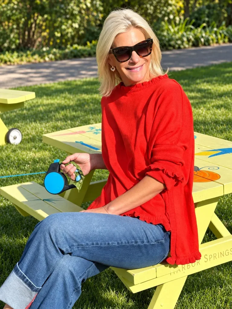 Angela Howenstein wearing a red long-sleeve top and cuffed jeans while seated outdoors.
