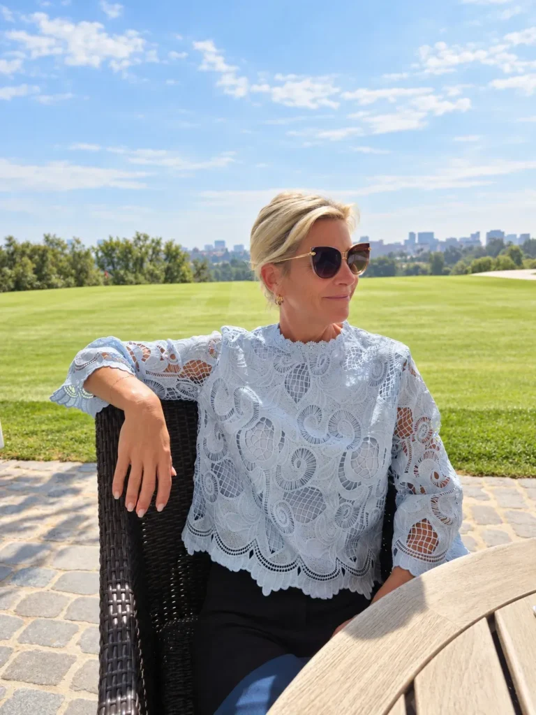 Angela Howenstein wearing a white lace blouse, dark trousers and sunglasses outdoors.