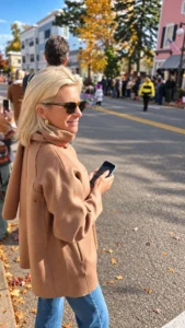 Angela Howenstein wearing a camel jacket and jeans on an autumn city street.