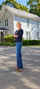 Angela Howenstein wearing a navy cardigan with blue jeans and tan flats outside a house.
