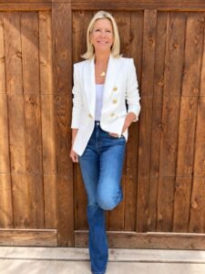 Angela Howenstein wearing a white double-breasted blazer over a white top with blue jeans.