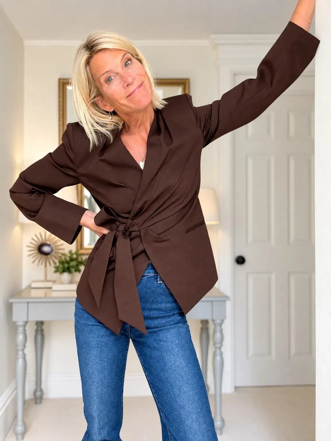Angela wearing a dark wrap blazer tied at the waist with blue jeans.