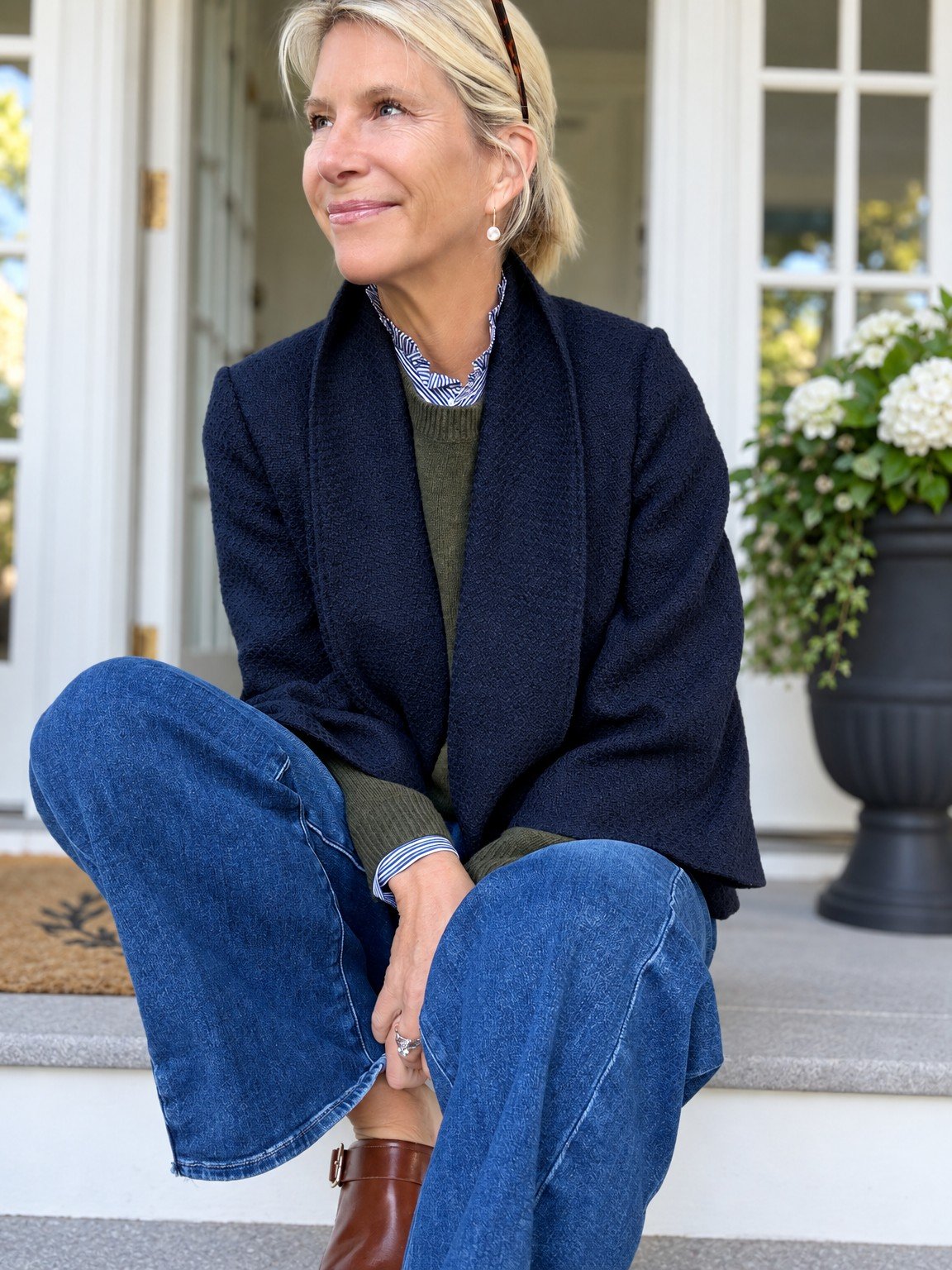 Angela seated in a navy textured jacket over green and striped layers with jeans.