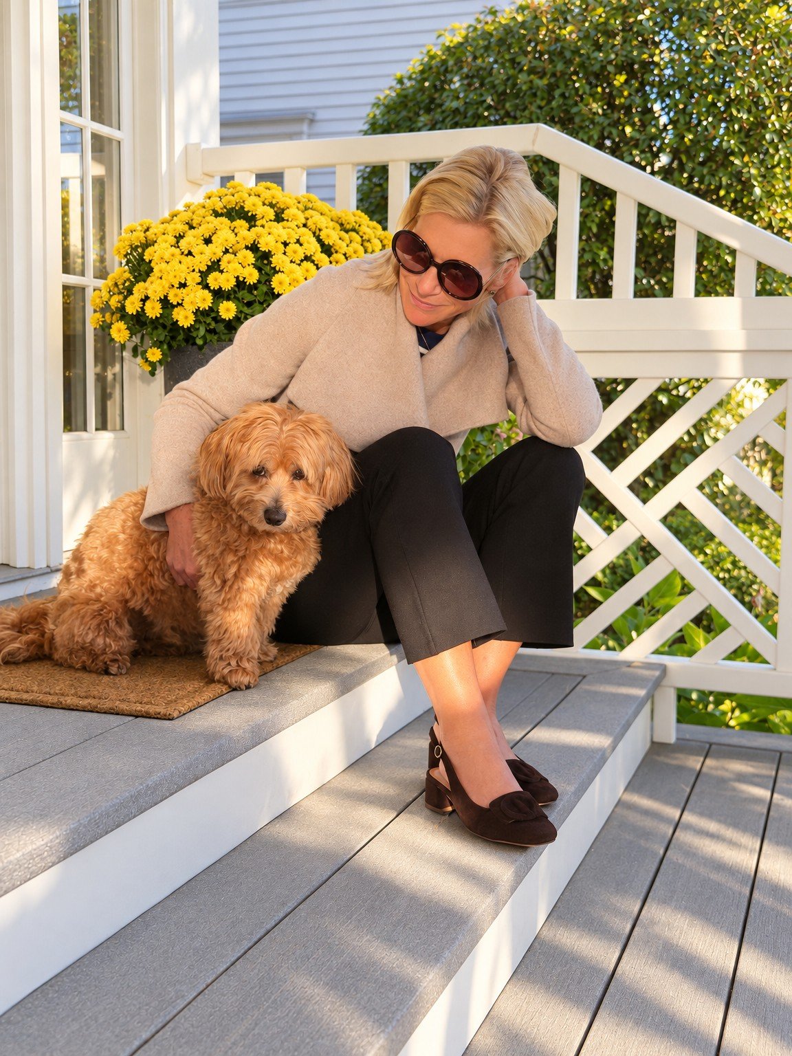 Angela wearing a Quince draped-collar wrap coat beside Rover on the front steps.
