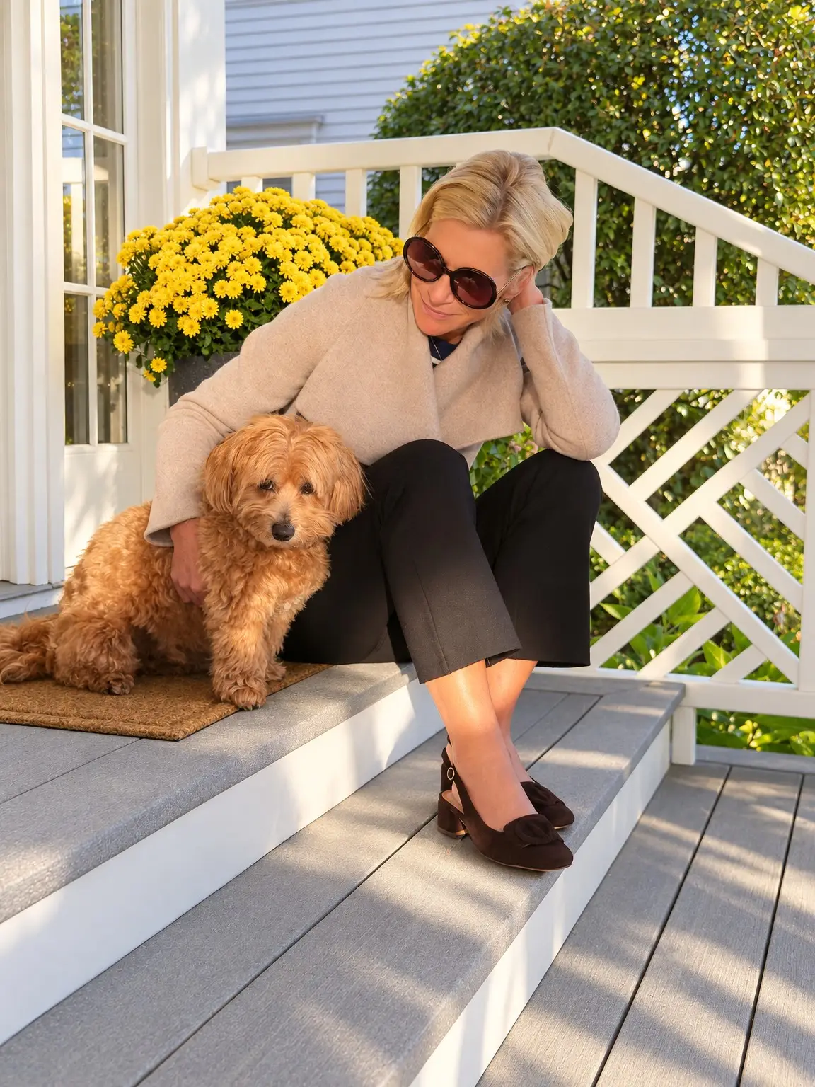 Angela wearing a beige jacket, seated beside her dog on the front steps.